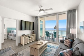 A modern living room with a flat-screen TV, a wooden coffee table, a sofa, and a balcony with a view of the ocean.