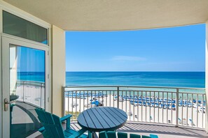 A balcony with a view of a beach, a table, and chairs.