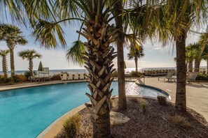 A pool area with lounge chairs and palm trees, overlooking a body of water.