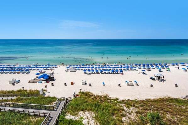 A beach with rows of umbrellas and sun loungers, a sandy shore, and a clear blue sea. - 506 - Beach Oasis Perfect for Families and Couples (Panama City Beach)