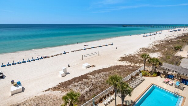 Ett semesterhotell vid stranden med en pool, solstolar och en brygga.