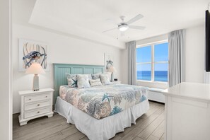 A bedroom with a bed, nightstands, a ceiling fan, a window with a view, and artwork on the walls.