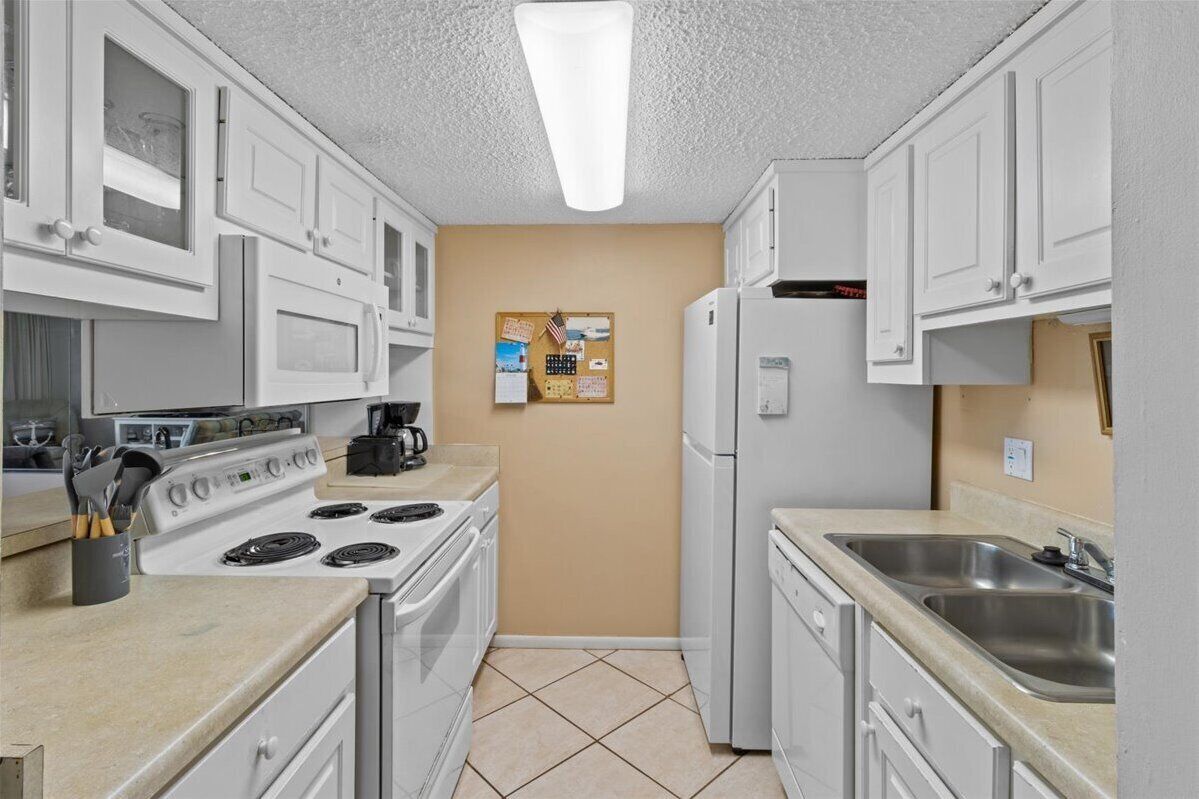 Una cocina compacta con armarios blancos, estufa, refrigerador y pileta.