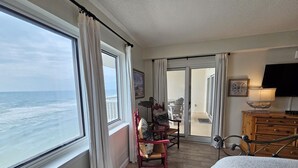 A room with a large window overlooking the ocean, a bed, a chair, a small table with a lamp, and a wooden dresser. - Sandy Key 615:  2 BR / 2 BA Gulf Front Condo in Perdido Key, FL  Sleeps 6 (Pensacola)