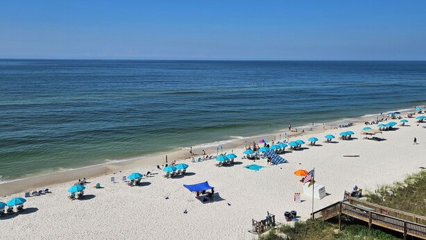 A beach with numerous blue umbrellas, a sandy shore, and a wooden walkway leading to the water. - Sandy Key 615:  2 BR / 2 BA Gulf Front Condo in Perdido Key, FL  Sleeps 6 (Pensacola)