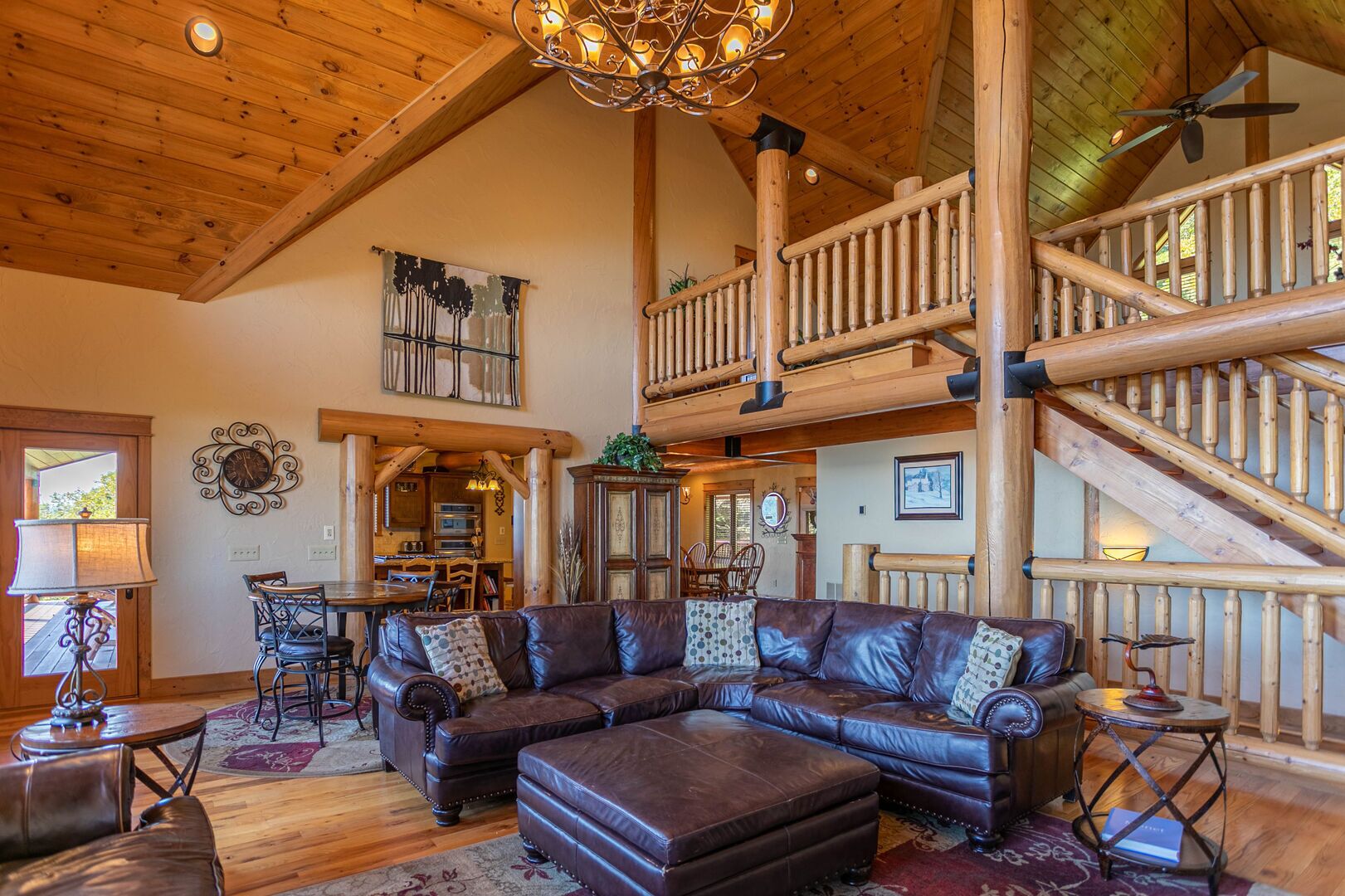 A spacious living room with a large L-shaped leather sofa, wooden flooring, and a high ceiling with exposed beams.