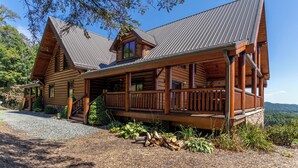 A log cabin with a porch, a chimney, and a view of the surrounding forest. - The Lodge - Theater Room, Putting Green, Pool, Great view 2 miles to Boone! (Boone)