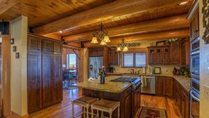A spacious kitchen with wooden cabinets, a granite countertop, and a central island with stools. - The Lodge - Theater Room, Putting Green, Pool, Great view 2 miles to Boone! (Boone)