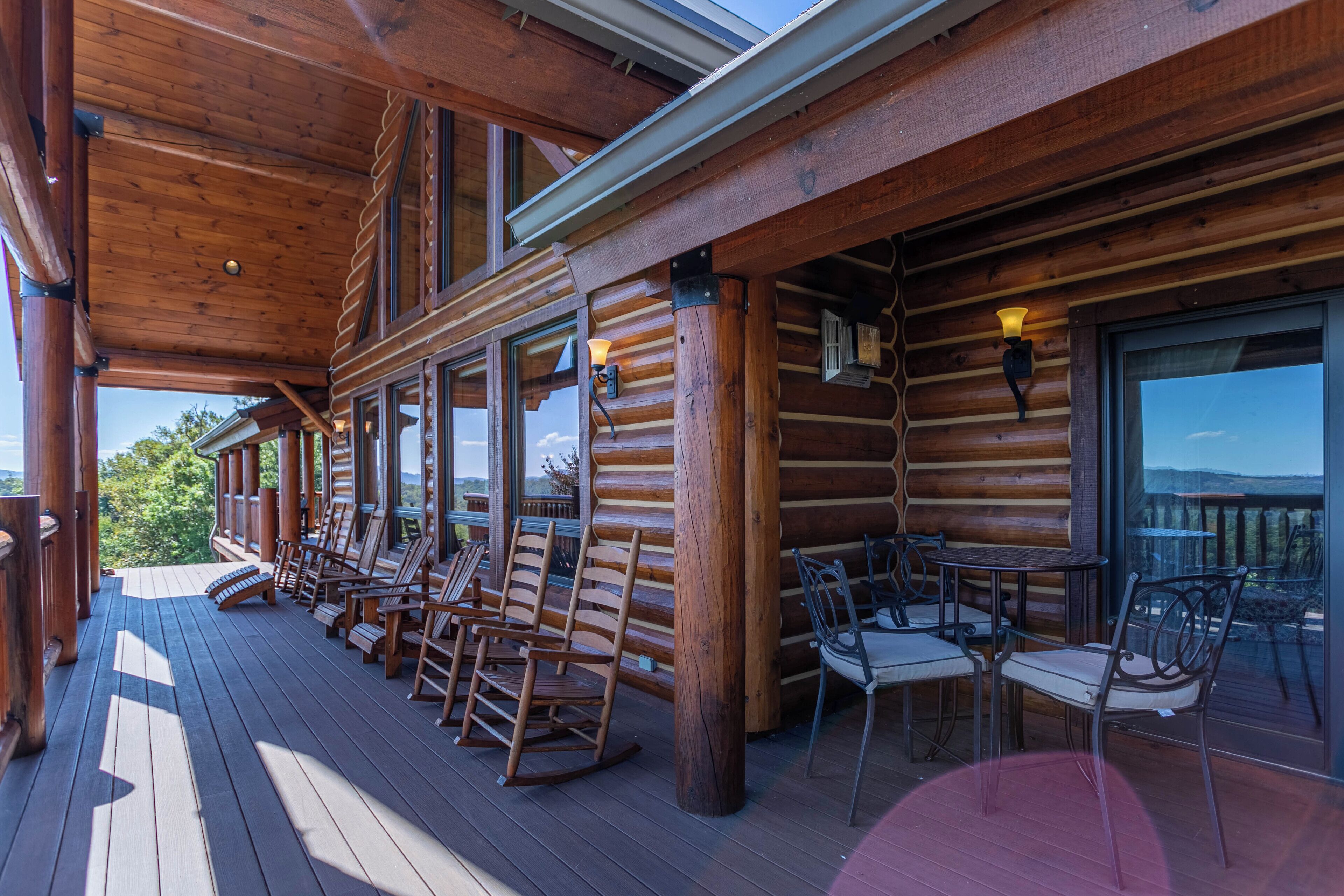 A wooden deck with rocking chairs and tables, large windows, and a view of the landscape.