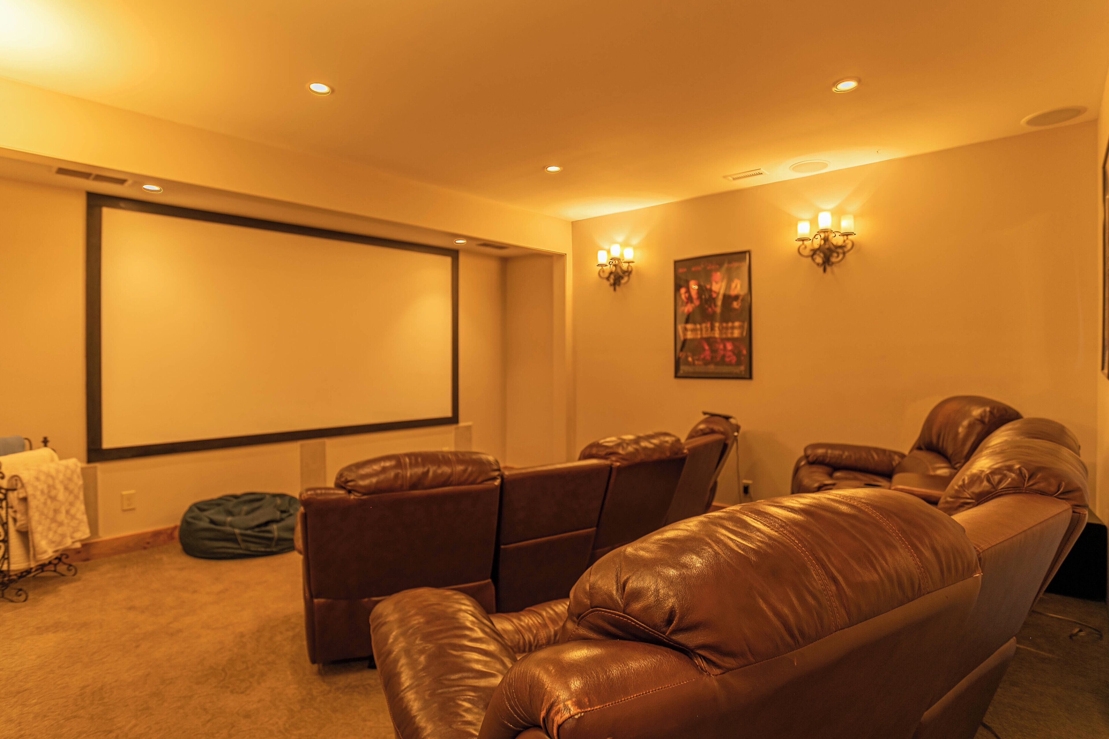 Una sala de cine en casa con una pantalla grande, asientos reclinables de cuero e iluminación empotrada.