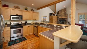 Une cuisine avec des meubles en bois, un plan de travail en granit, un four encastré et une cheminée en pierre.