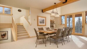 Un coin repas avec une table et des chaises en bois, un escalier et une grande fenêtre donnant sur les arbres.