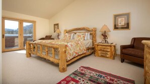 Une chambre à coucher avec un lit en bois, un tapis rouge à motifs, un fauteuil en cuir marron et une table de chevet en bois.