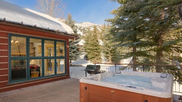 Une cabane en bois dotée de grandes fenêtres, d’un bain à remous et surplombant un paysage montagneux enneigé.