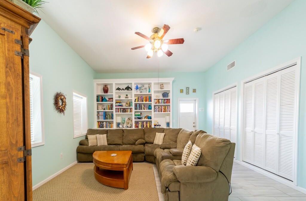 A living room with a sectional sofa, a coffee table, a ceiling fan, and a bookshelf.