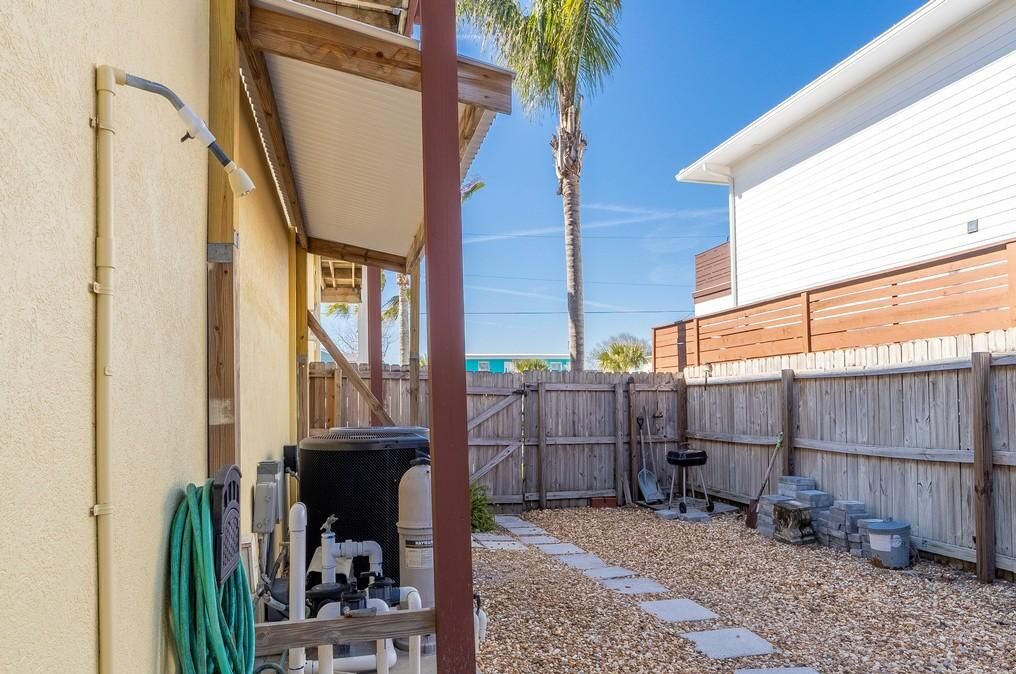 A backyard with a wooden fence, a palm tree, and a gravel path.