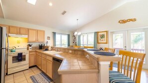 A spacious kitchen with wooden cabinets, a central island, and a dining area with a chair. - Ocean View Pool Home ~ Heated Pool ~ Steps to the Beach! (Saint Augustine)