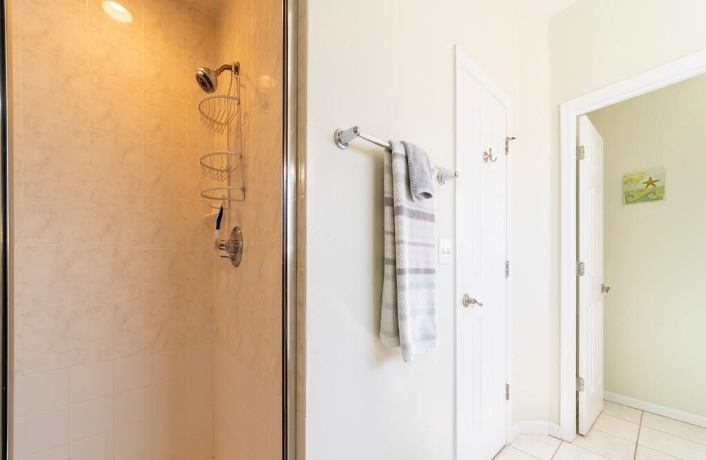 Un baño con cabina de ducha de vidrio, una puerta blanca con una toalla colgada en un perchero y un pequeño adorno en la pared.