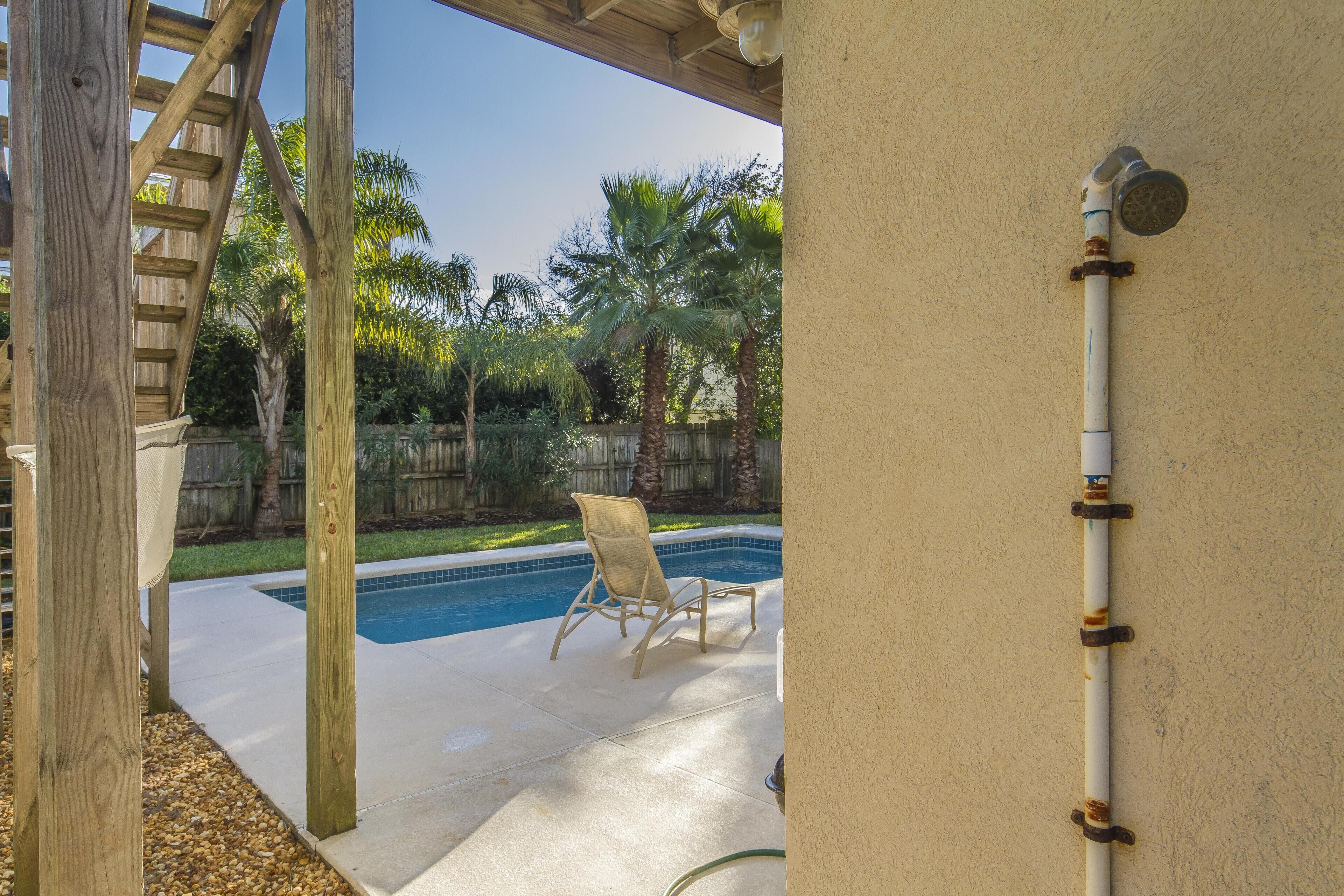 A pool area with a wooden pergola, a lounge chair, and a water pipe.