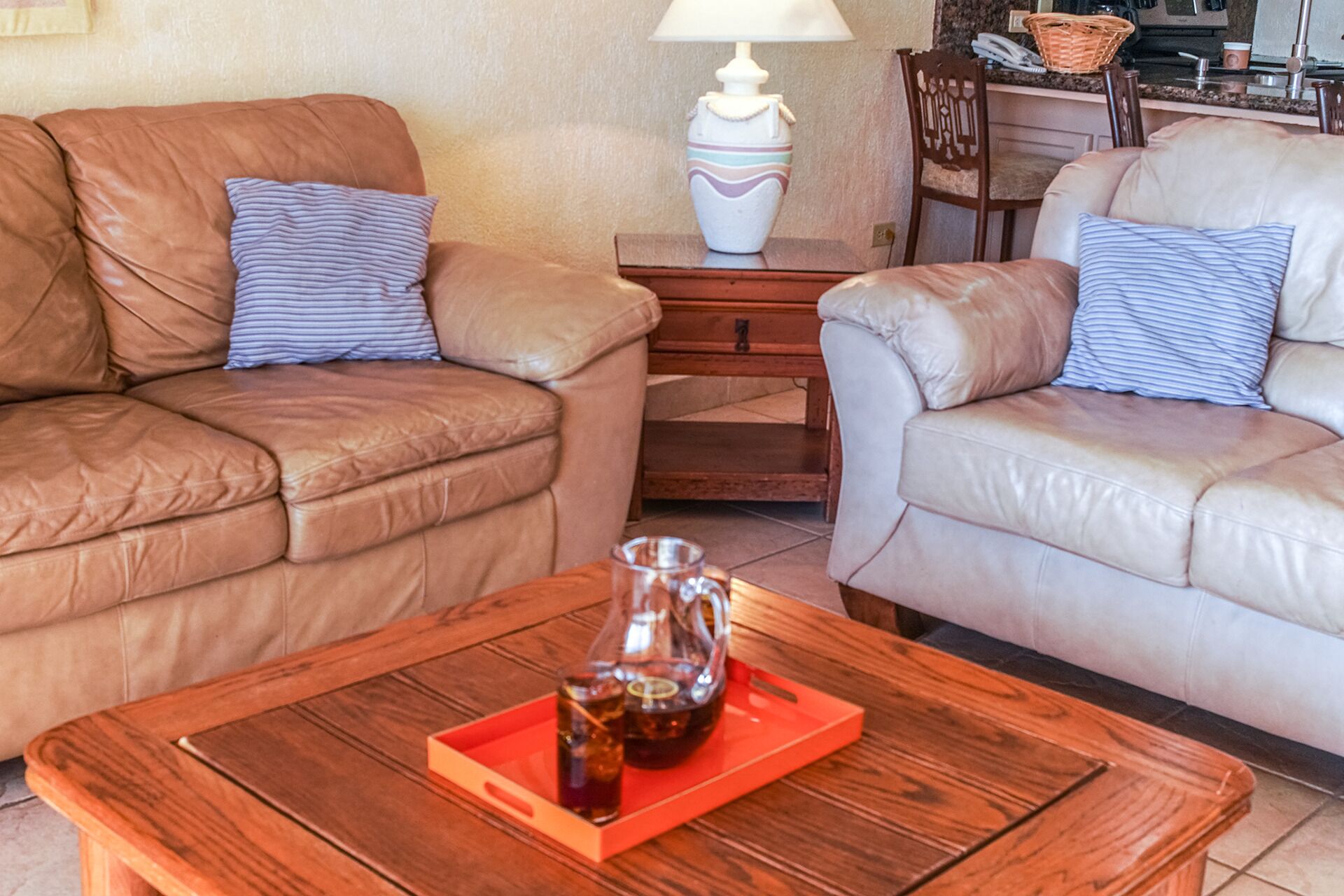 Un salon avec deux canapés en cuir, une table basse en bois sur laquelle se trouve un plateau avec des bouteilles, et une lampe sur une table d’appoint.