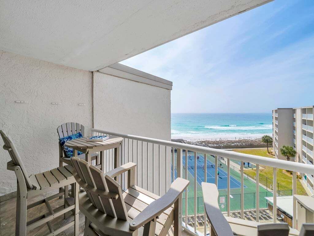 Un balcon avec des chaises et une table donnant sur un court de tennis et une plage.