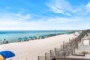 A beach with rows of umbrellas and sun loungers, a wooden fence, and a clear view of the ocean. - 715- Perfect Family Top Floor Condo - with Stunning Ocean and Beach Views (Destin)