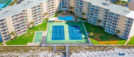 A multi-story hotel with a tennis court, pool, and beach area.