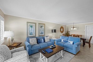 Un salon avec deux canapés bleus, une table basse et un coin repas agrémenté d’un lustre.