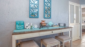 A reception desk with a sign reading "Welcome to our Beach House," a decorative fish, a calendar, and a vase.