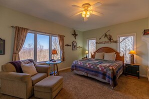 Une chambre confortable avec un grand lit, une chaise, une petite table et un ventilateur de plafond.
