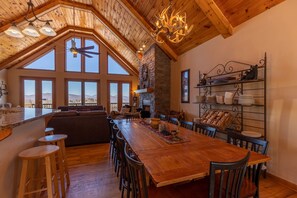 A spacious dining area with a long wooden table, multiple chairs, and a stone fireplace.