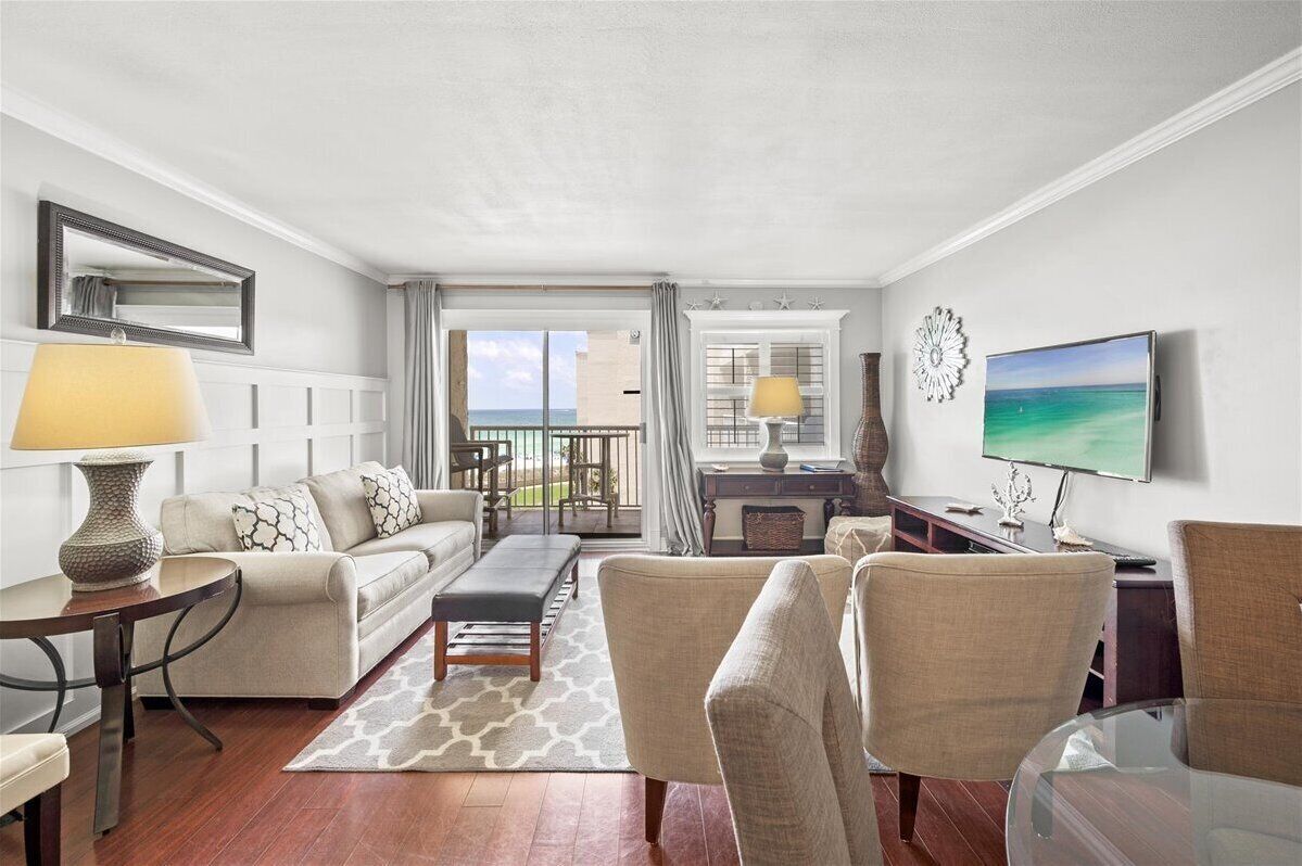 Ein modernes Wohnzimmer mit einer Couch, Sesseln, einem Couchtisch und einem Fernseher. Ein Balkon bietet Blick auf den Ozean.