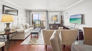 A modern living room with a sofa, chairs, a coffee table, and a TV. There is a balcony with a view of the ocean. - 513- Modern Coastal, updated beachfront Condo with Incredible Gulf views! (Destin)