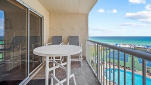 A balcony with a white table and chairs, overlooking a pool and beach area. - 513- Modern Coastal, updated beachfront Condo with Incredible Gulf views! (Destin)