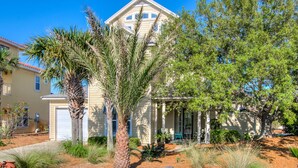A two-story house with a beige exterior, a covered porch, and a well-maintained garden with various plants and a palm tree.