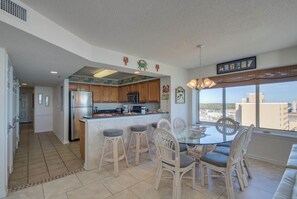 A modern kitchen with a central island, wooden cabinets, and a view of the city through large windows. - Luxury oceanfront condo - Indoor/Outdoor Pools + Free Attraction Tickets! (North Myrtle Beach)