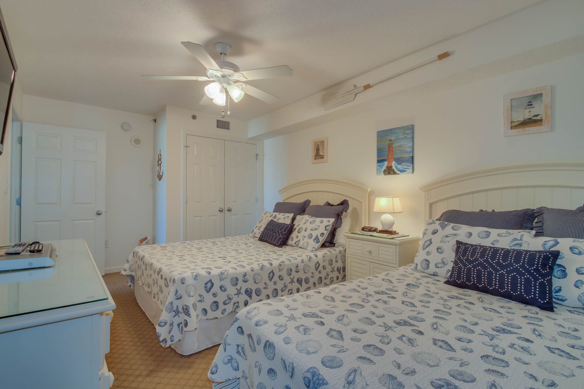 A bedroom with two beds, a ceiling fan, a nightstand, and a wall-mounted lamp.