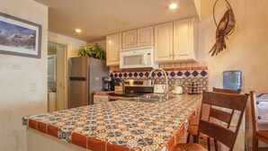 A kitchen with a tiled island, wooden cabinets, a microwave, a refrigerator, and a water dispenser.