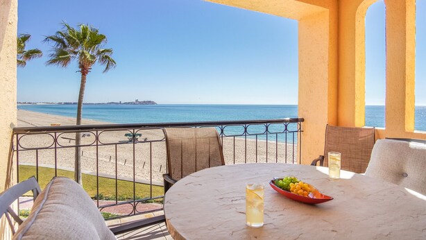 A balcony with a table, chairs, a drink, and a bowl of fruit.