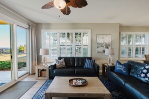 A living room with a black leather sofa, a wooden coffee table, and a ceiling fan. - 106E ~ Bright 3BR/3BA beautiful corner condo! (Gulf Shores)
