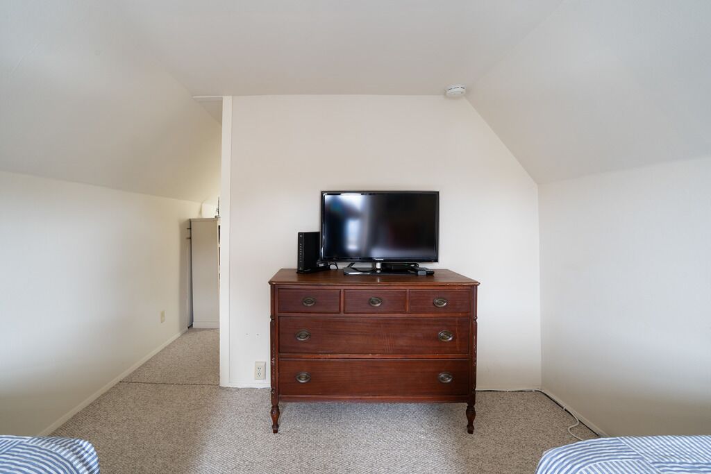 Una habitación con cómoda de madera, televisor de pantalla plana encima y piso alfombrado.