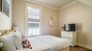 Ein Schlafzimmer mit Bett, Schminktisch, Fernseher und einem Fenster mit Jalousien.