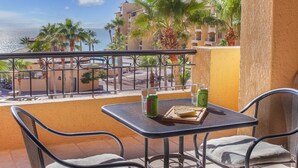 A balcony with a table and chairs, overlooking a beach and palm trees.