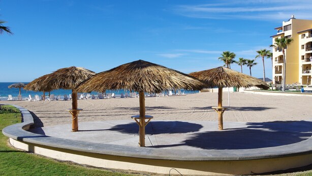 A beachside resort with thatched umbrellas, lounge chairs, and a building with balconies overlooking the ocean.
