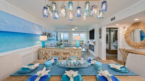 A dining area with a view of the ocean, a wooden ceiling, and a rustic dining table set with blue plates and napkins. - 202- Newly renovated upscale Gulf Front Condo, Includes FREE Beach Service (Destin)
