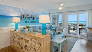 A room with a view of the ocean, a large 'DEJA ISLE BE SEAN' sign, a wooden cabinet, and a white chair by the window. - 202- Newly renovated upscale Gulf Front Condo, Includes FREE Beach Service (Destin)