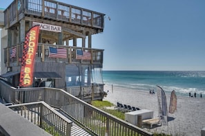 A beach bar with a wooden structure, American flags, and a lifeguard tower. - 2 Free Beach SRVCS- 4 chairs/2 umbrellas! Free Beach Bonfires M/F nts (Miramar Beach)