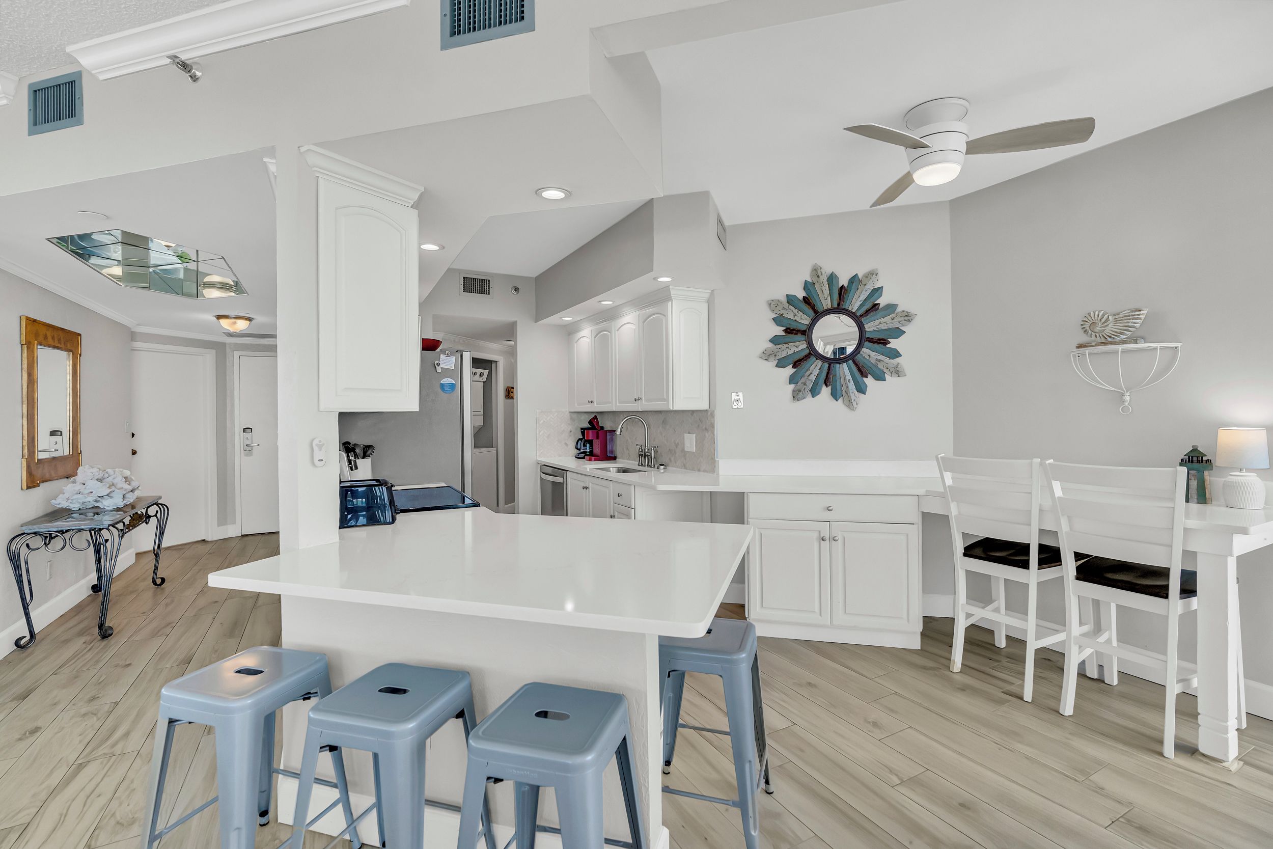 A modern kitchen with white cabinetry, a central island with stools, and a ceiling fan.