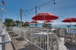 A deck with outdoor seating and red umbrellas, overlooking a beach. - 2 Free Beach SRVCS- 4 chairs/2 umbrellas! Free Beach Bonfires M/F nts (Miramar Beach)