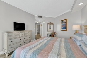 Een slaapkamer met een bed, een dressoir, een televisie en kunstwerken.